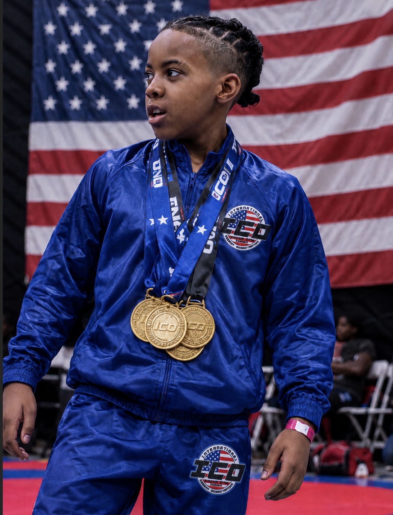 Champ standing full length in a blue Team USA tracksuit wearing medals in front of an American flag